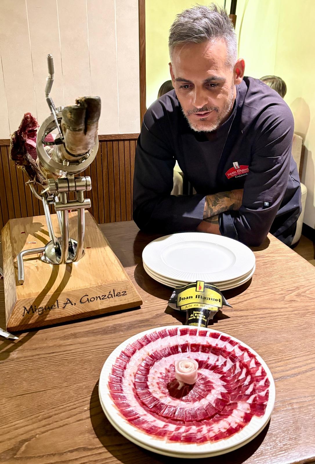 Miguel Ángel González junto a su soporte de corte grabado con su nombre, presentando una pieza de jamón ibérico